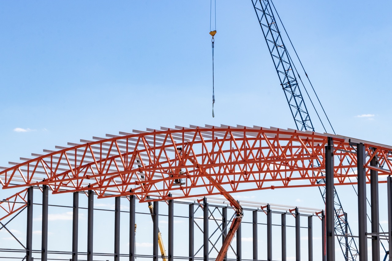 Installation of metal trusses and frame during the construction of an industrial building or factory. The work of installers during the installation of the roof. Construction of a large frame shop
