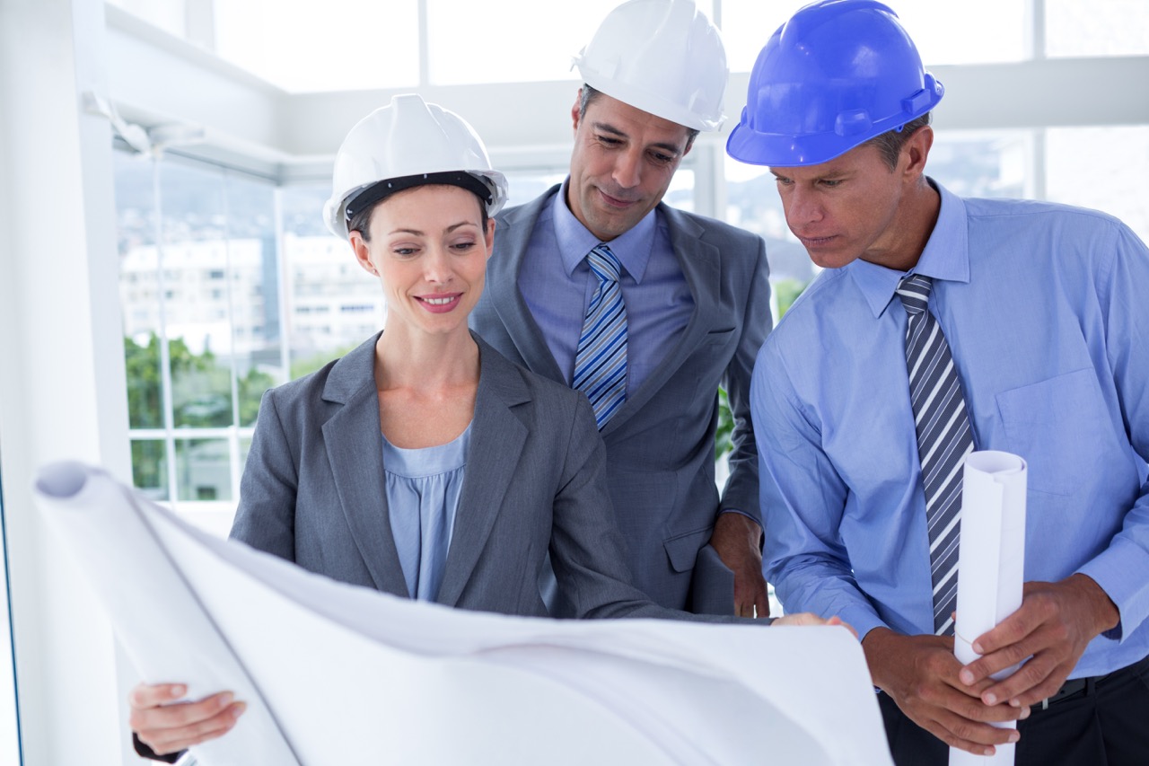 Businessmen and a woman with hard hats and holding blueprint in the office